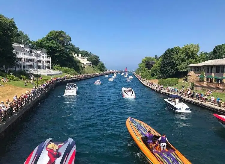 A crowded waterway lined with spectators and houses, with numerous motorboats approaching the camera.