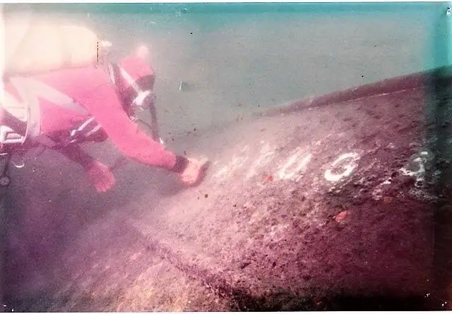 A scuba diver marks white lettering on a dark underwater surface.