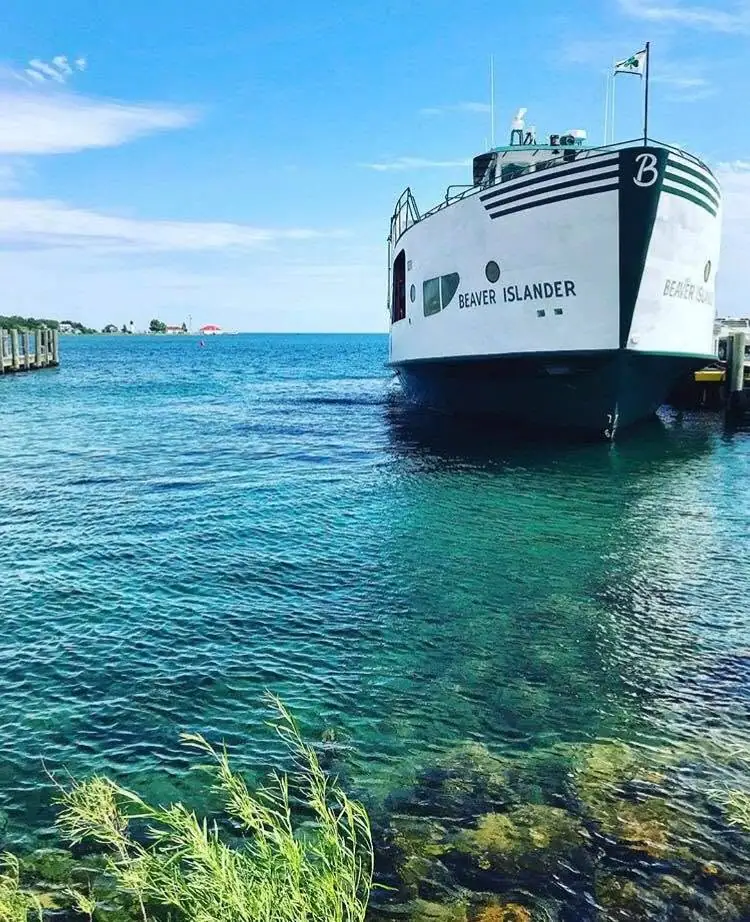 A white ferry named BEAVER ISLANDER sits beside a pier in clear blue water.