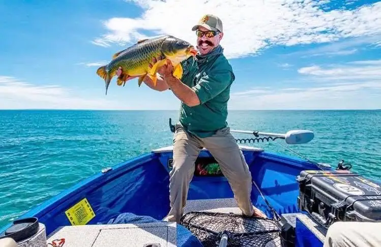 Angler holding a large fish aboard a blue boat on open water.