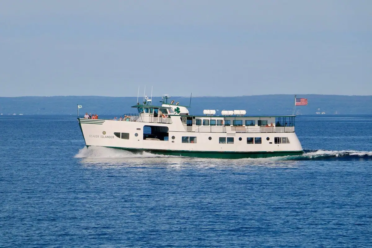 A white-and-green passenger ferry travels across open water with distant hills behind it.