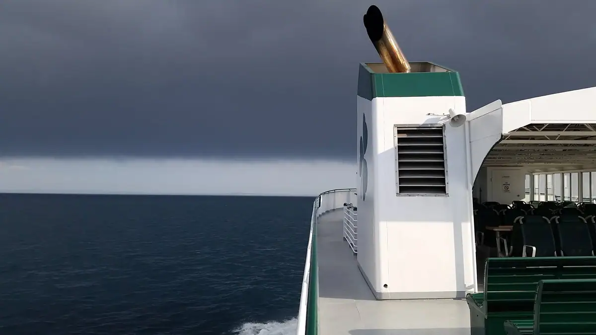 A passenger vessel’s deck shows a copper exhaust pipe, ventilation grille, and covered seating beside open water.
