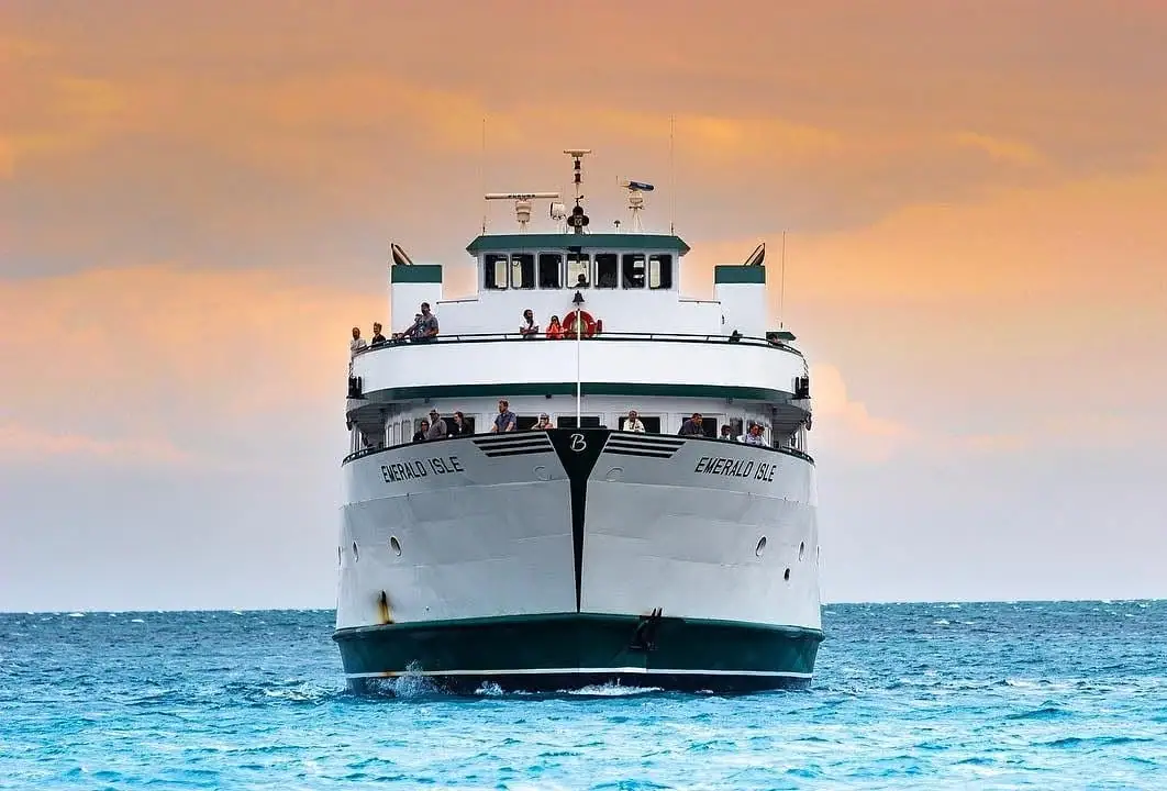 Front view of a white passenger ferry with green trim moving across choppy water.