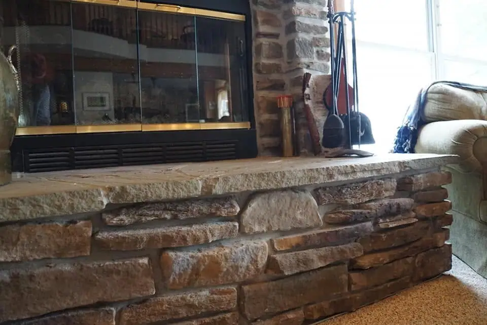Stone hearth with a glass-front fireplace, fireplace tools, and a sofa beside a bright window.
