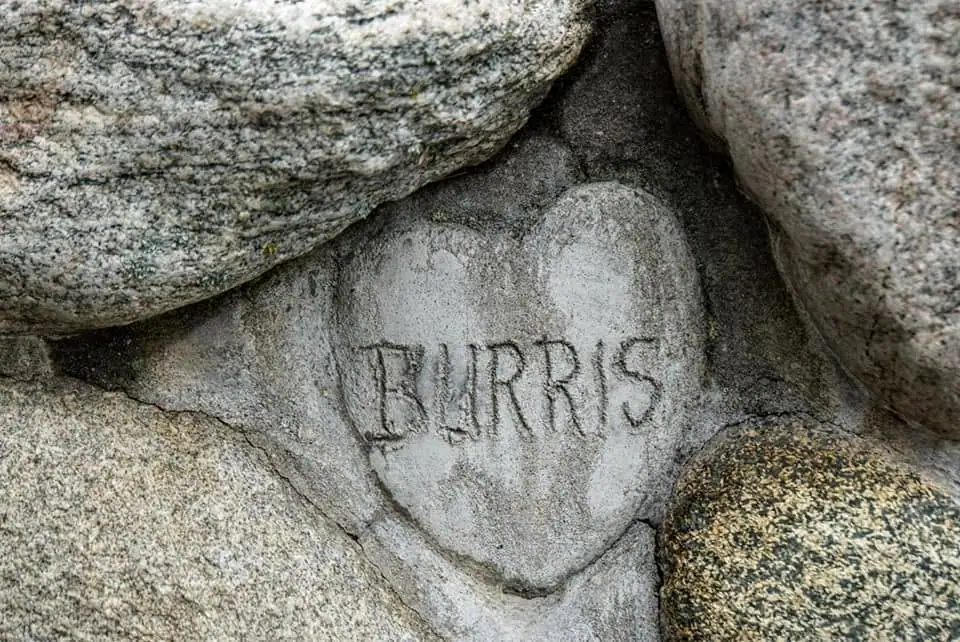 A heart-shaped stone carved with “BURRIS” is set among larger rough stones.