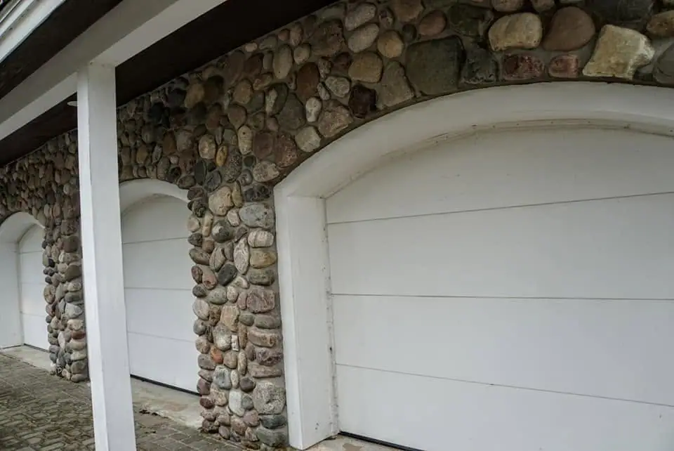 Three white garage doors are set beneath rounded arches faced with multicolored fieldstone.