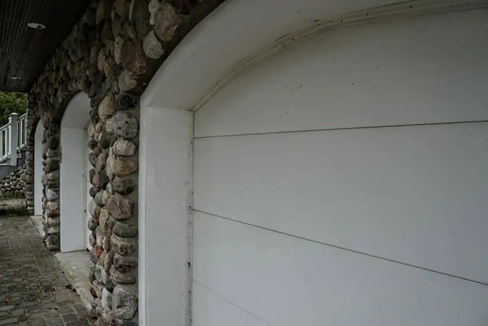 Exterior wall of rounded fieldstone with white arched doors beside a paved walkway.