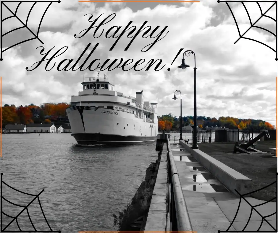 A white ferry approaches a pier beneath a Halloween greeting and decorative spiderweb border.