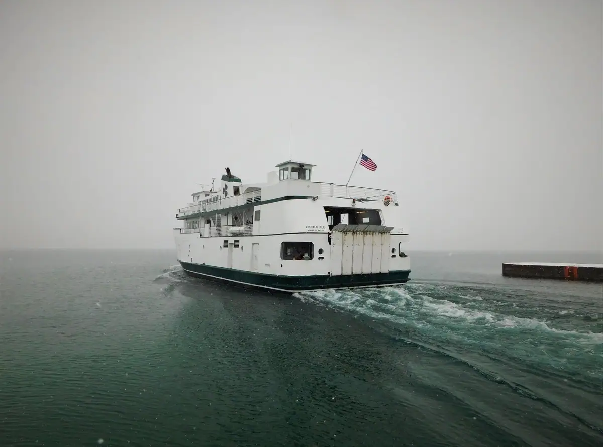 A white passenger ferry moves through snowy water beside a pier, leaving a broad wake.