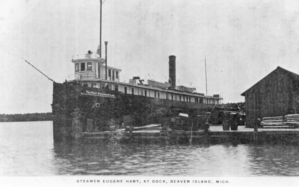 Black-and-white photograph of a large steamer moored beside a wooden dock and waterfront shed.