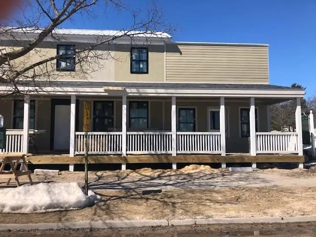 A two-story building with a broad porch stands beside snow-covered ground and a leafless tree.