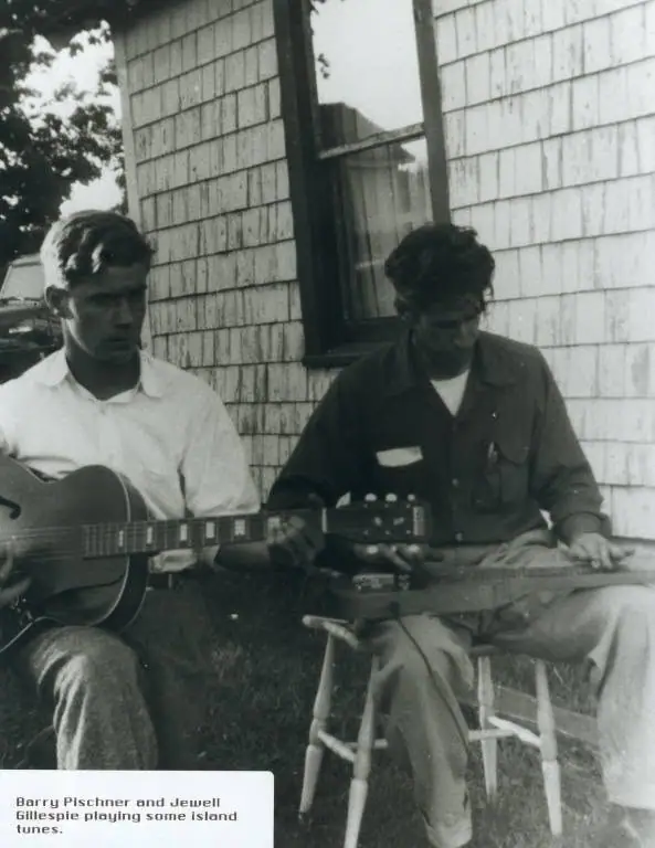 Two men seated outdoors play guitars beside a shingled building, with a printed caption at lower left.