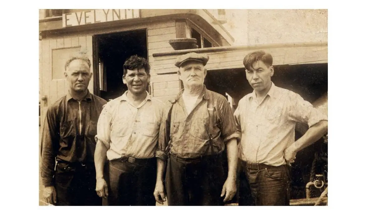 Four men stand outside a wooden building marked “EVELYN.”