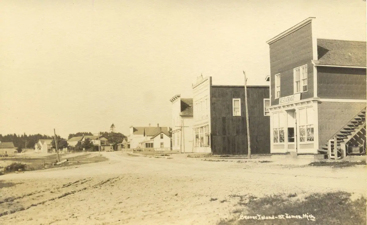 A broad unpaved street lined with wooden buildings, including a storefront marked “RESTAURANT.”