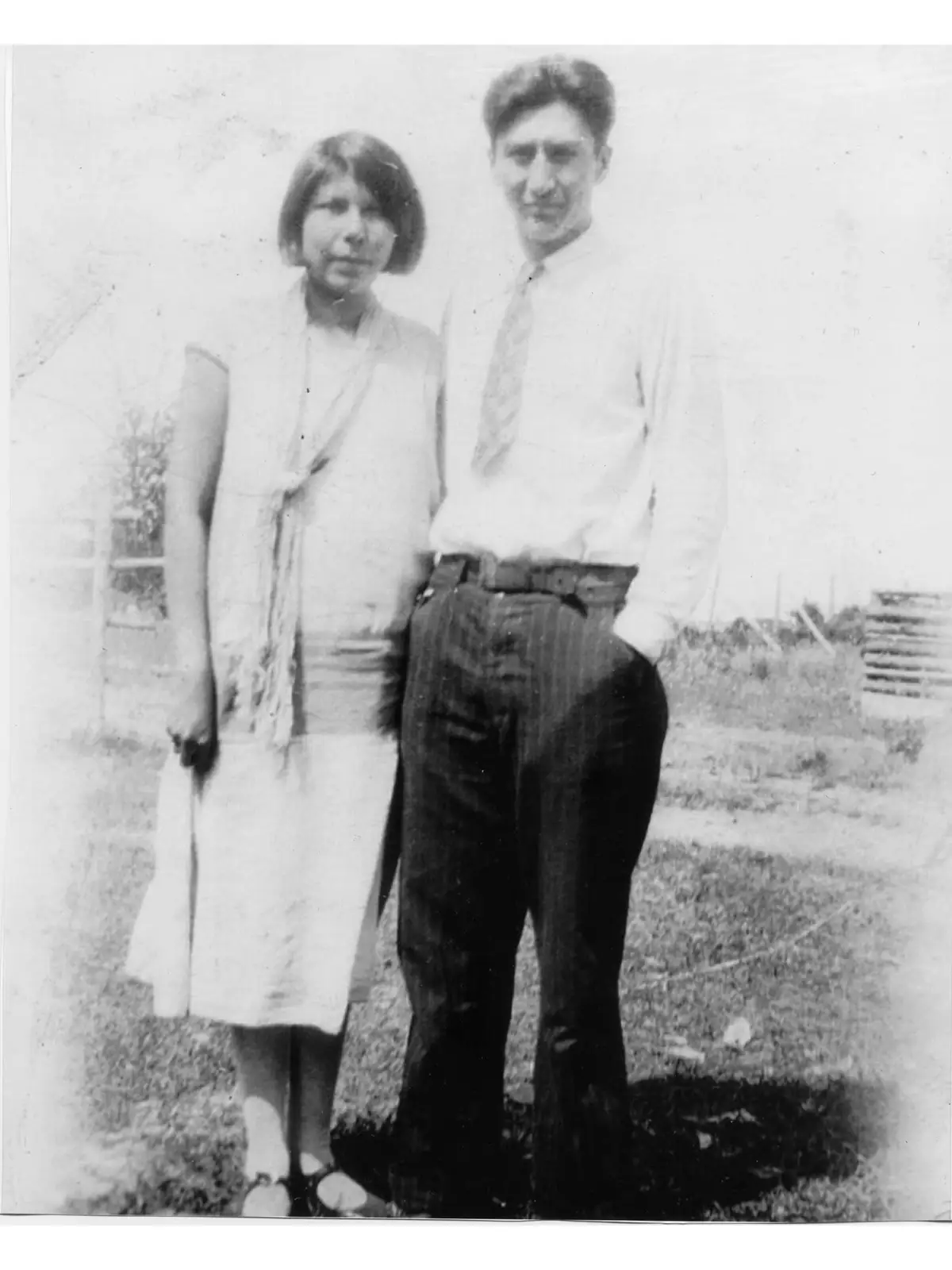 Black-and-white portrait of a woman and man standing outdoors in front of a yard and fencing.
