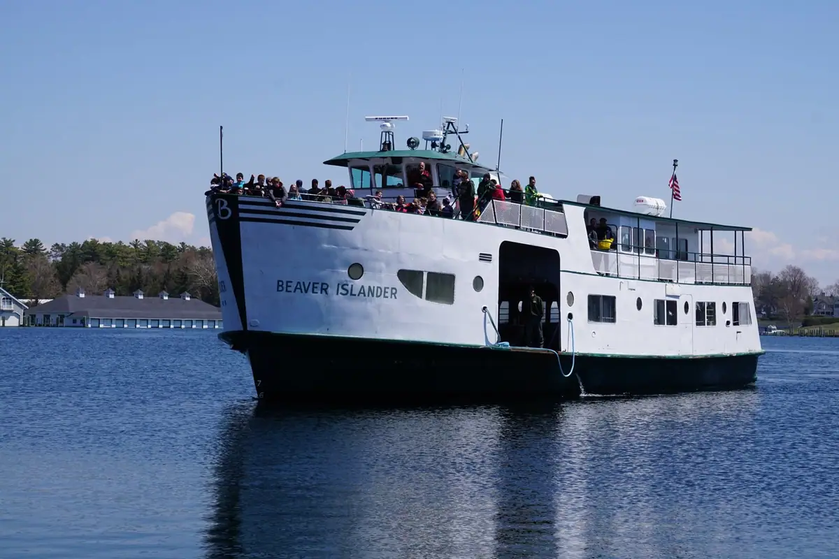 Passenger ferry carrying people passes a wooded shoreline, with its hull name visible.