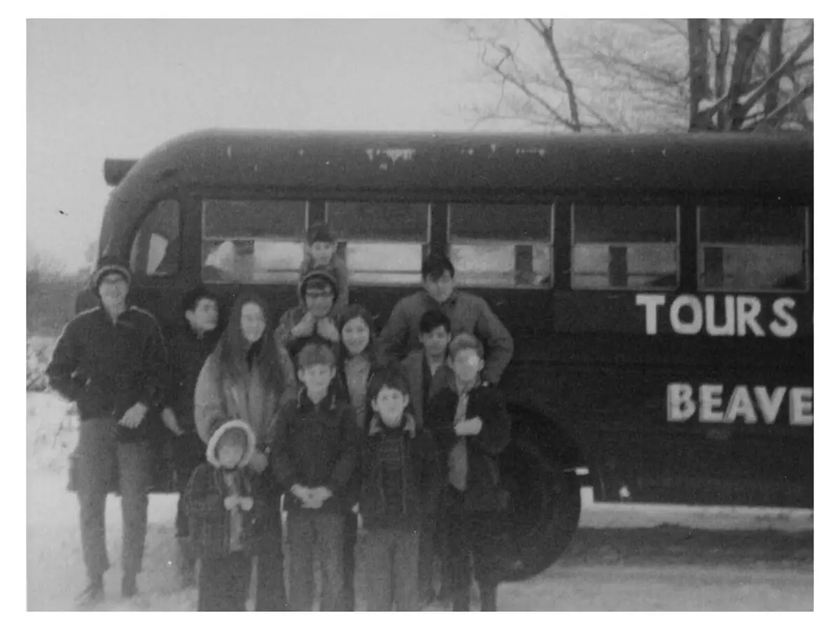 A group of people poses in front of a bus marked “TOURS” and “BEAVE” in a snowy setting.