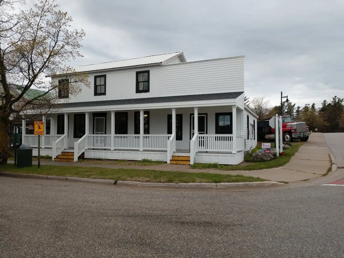 A white two-story building with a broad porch, a red truck, and roadside warning and business signs.