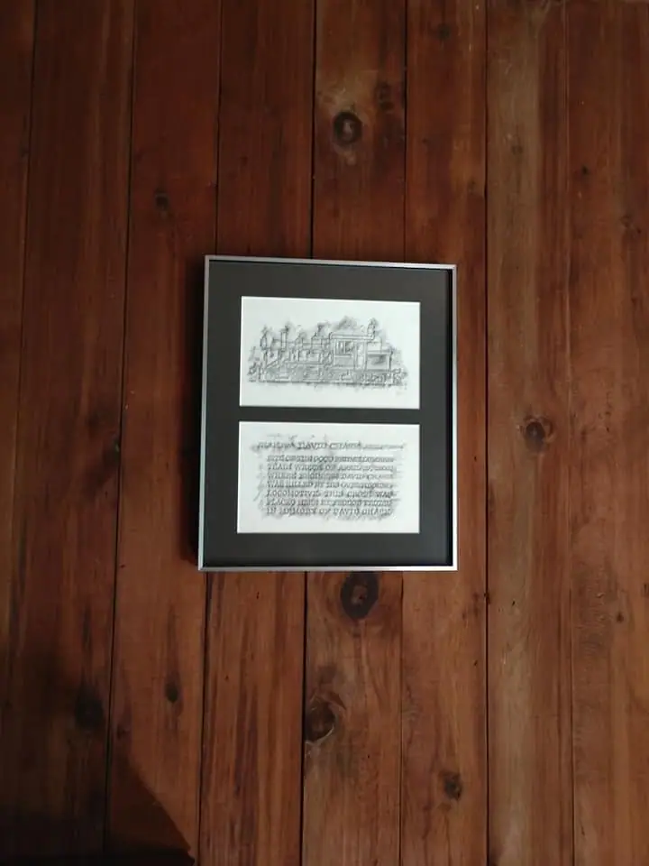 Photograph of a framed illustrated plaque mounted on a wood-paneled wall.