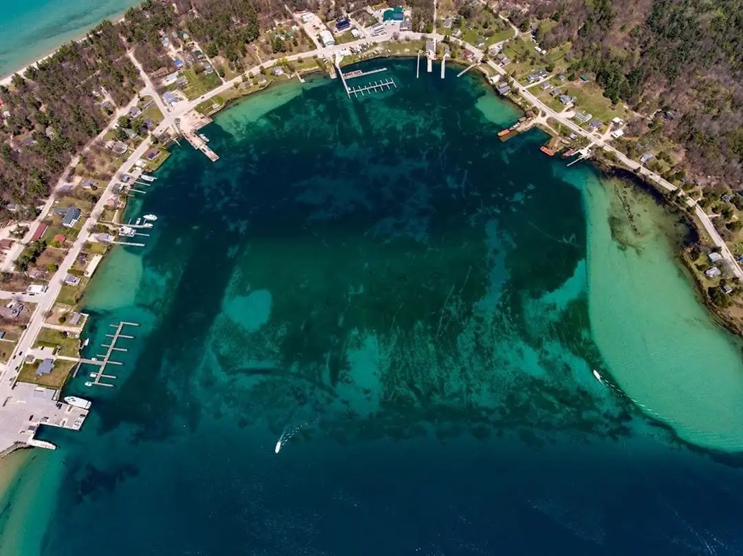 Aerial view of a sheltered harbor with docks, boats, homes, roads, and wooded shoreline.
