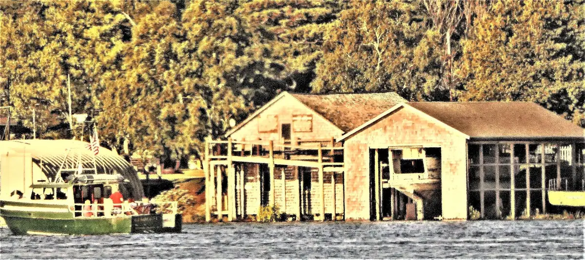 A green-and-white covered boat moored beside wooden waterfront buildings and dense trees.