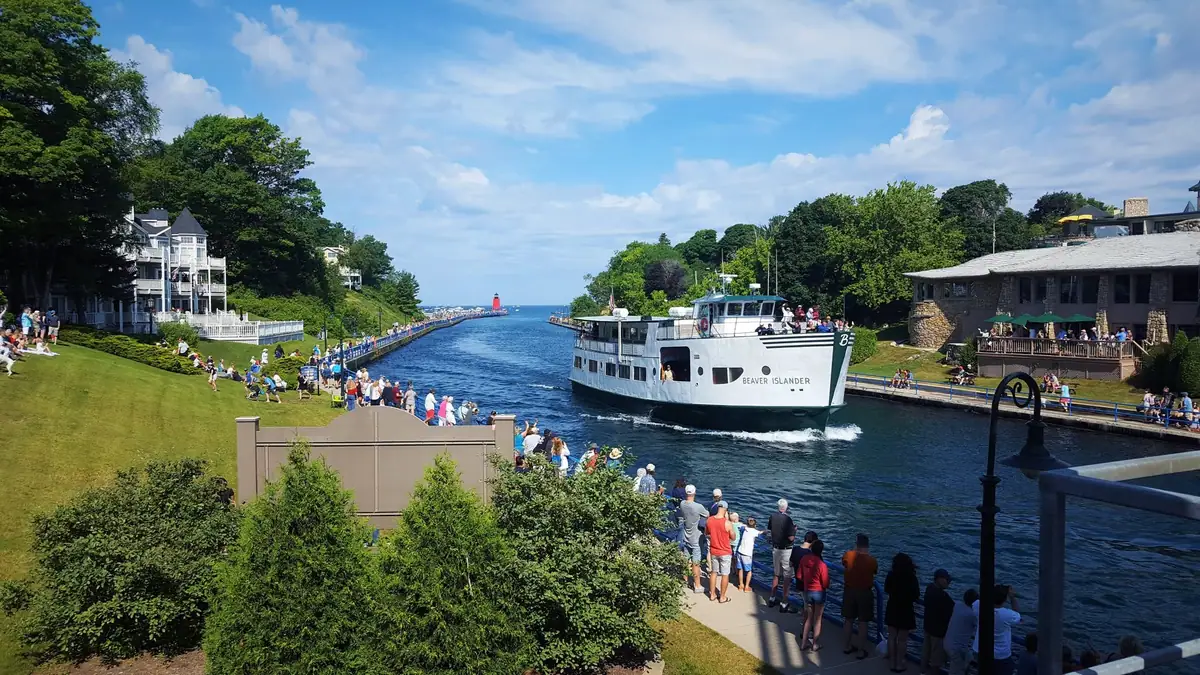 A white passenger ferry passes through a channel as crowds gather along both banks.