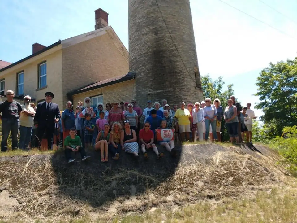 A large group poses on a grassy slope beside a brick building and a tall cylindrical tower.
