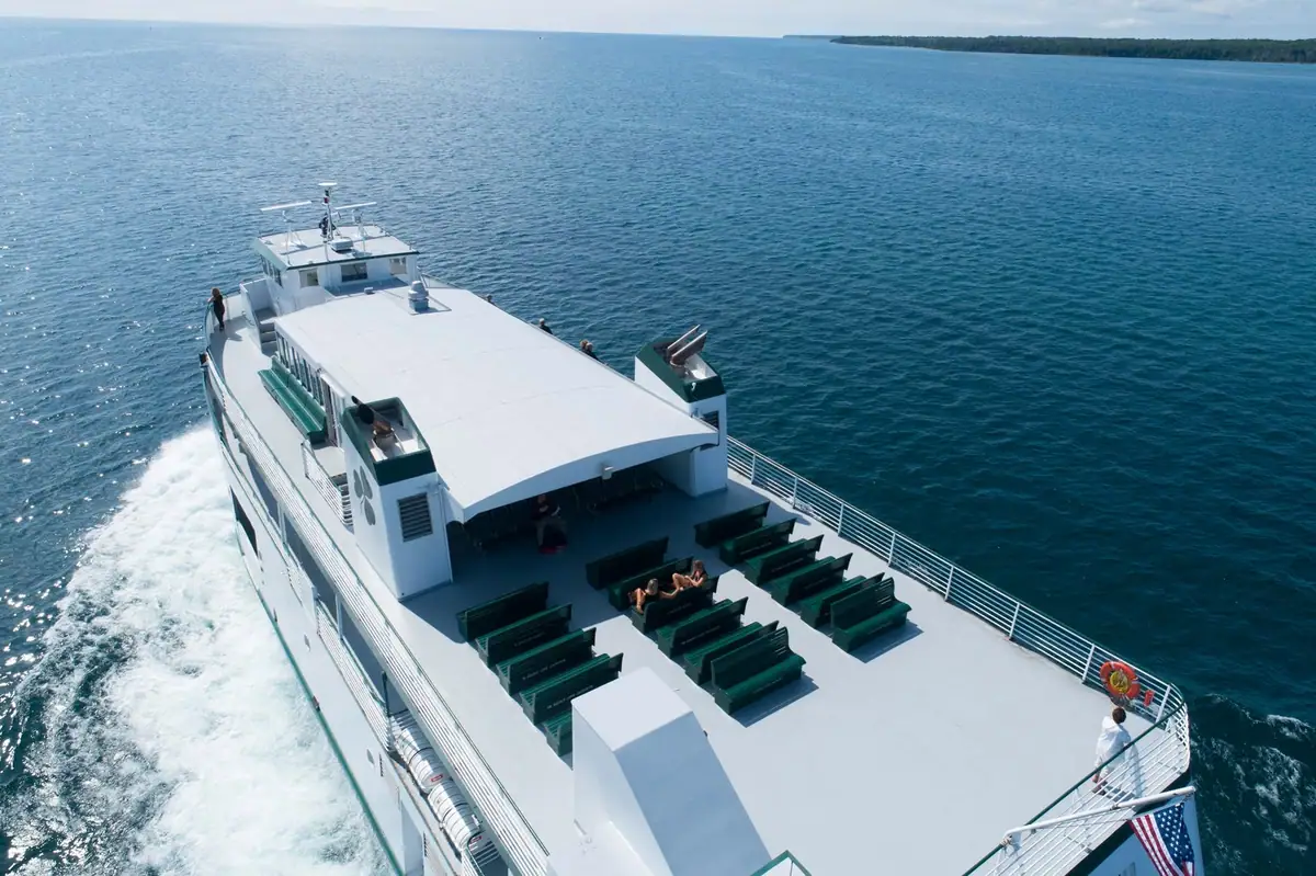 Aerial view of a white passenger ferry with green benches moving across blue water.