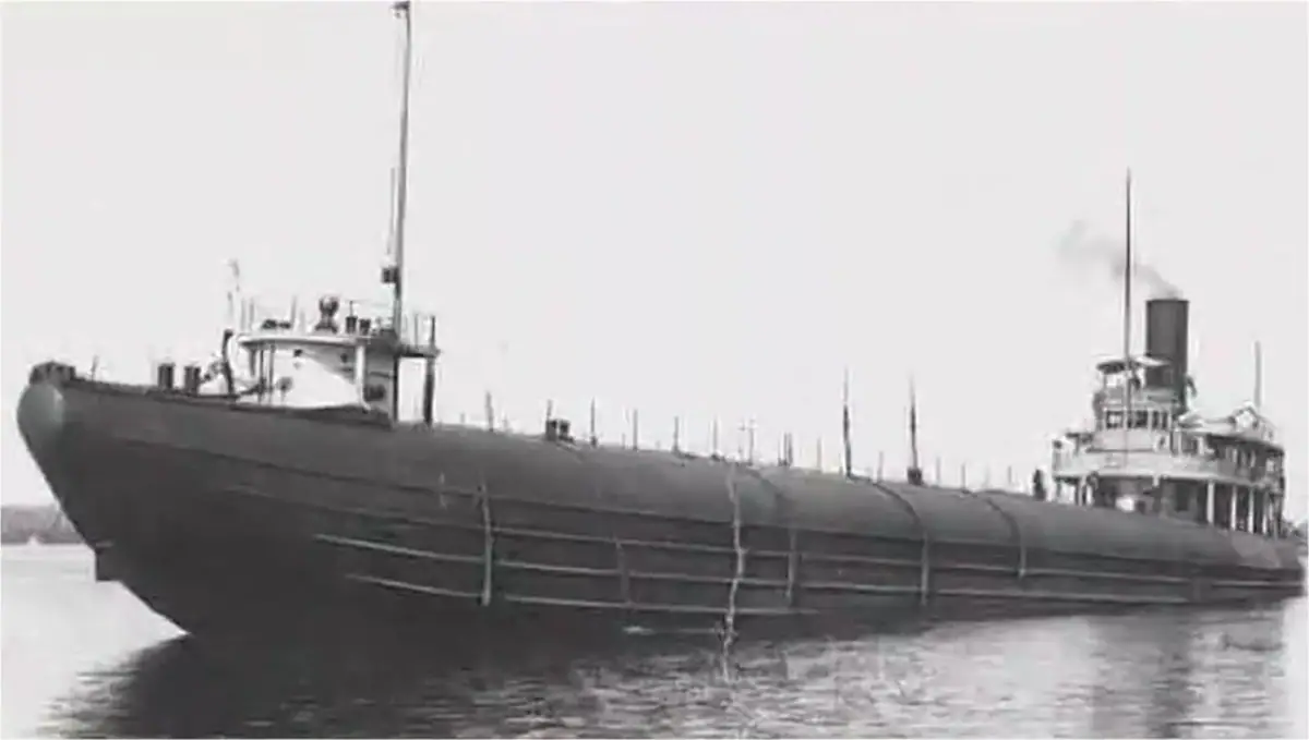 Black-and-white photograph of a large whaleback freighter underway on calm water, with smoke rising from its stack.