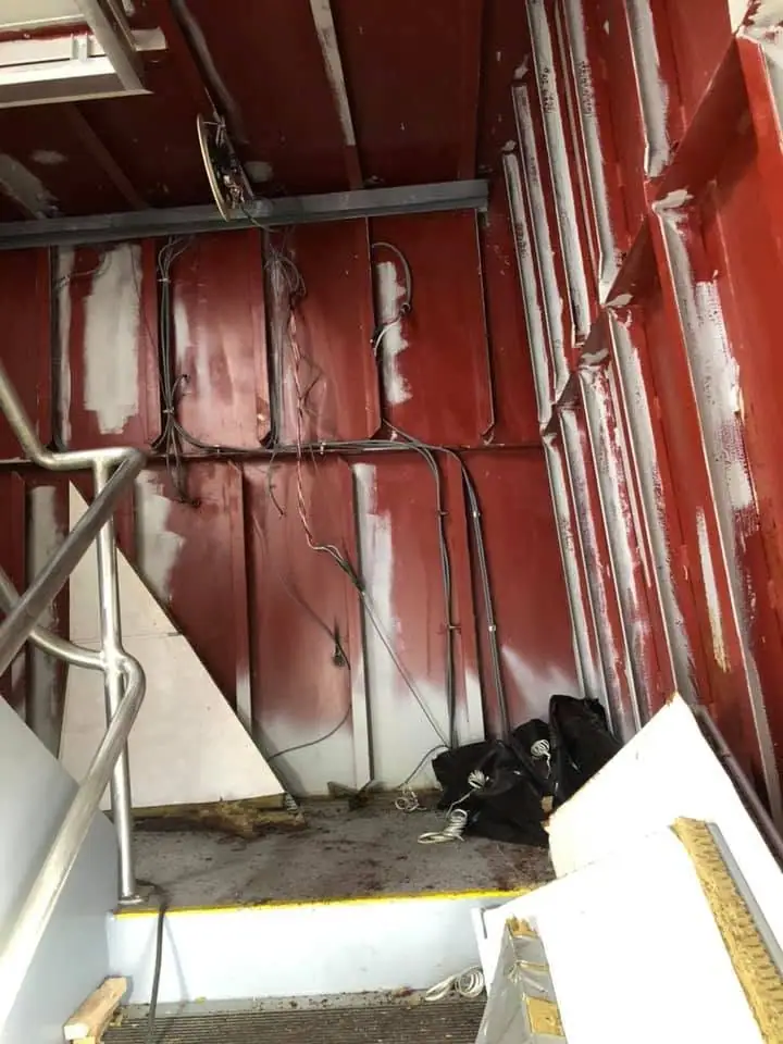 Red-painted metal interior with exposed wiring, pipes, a stair railing, and worn flooring.