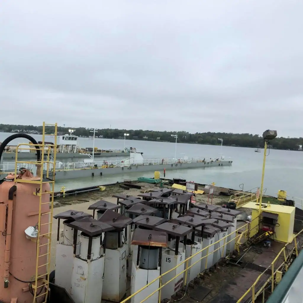 An industrial vessel is moored beside a water-filled dock, with machinery and tanks covering the foreground deck.