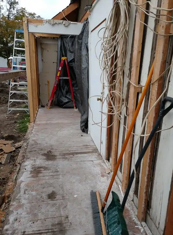 An unfinished structure with exposed framing, a concrete walkway, ladders, tools, and bundled cables.