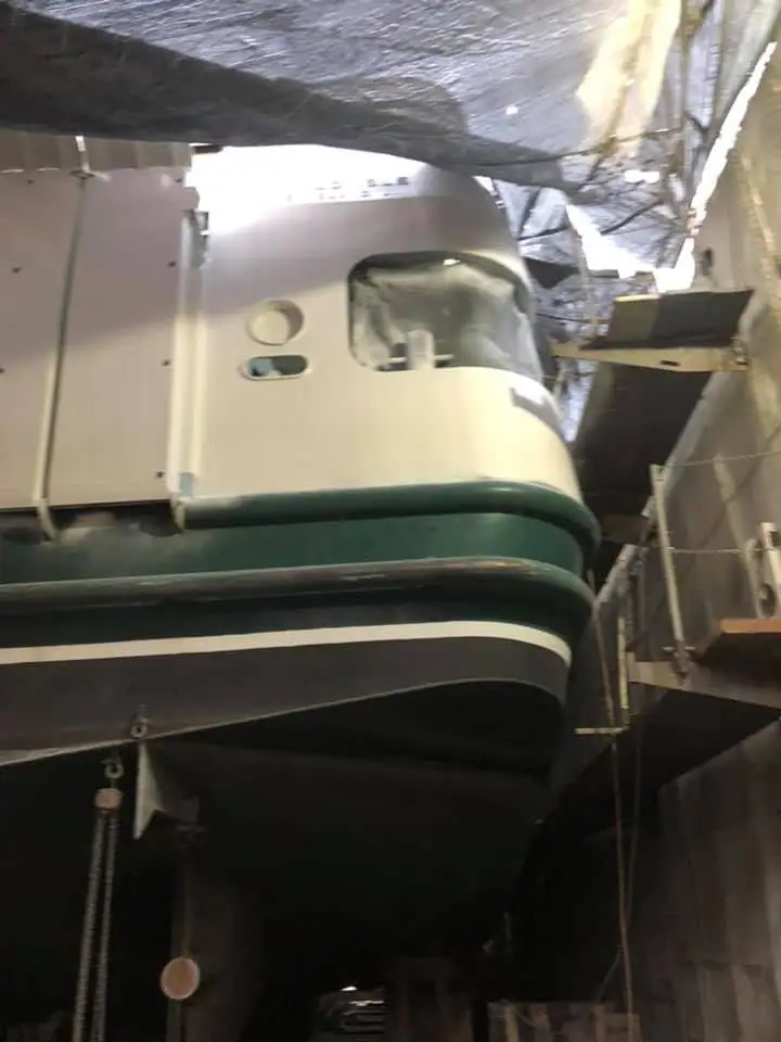 A white-and-green vessel is raised inside a covered workshop, with its hull exposed for repair.