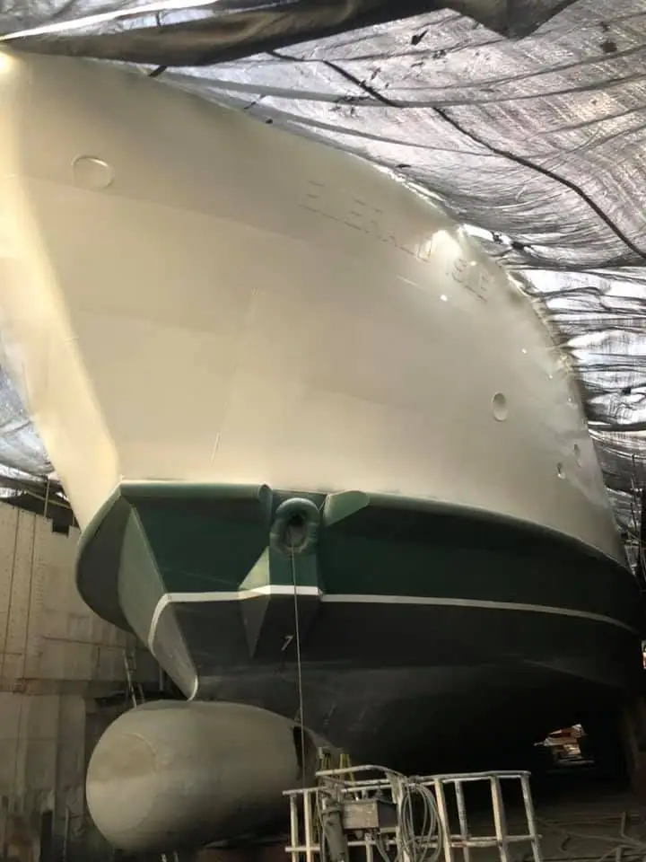 Close view of a vessel’s bow and dark lower hull inside a covered repair building.
