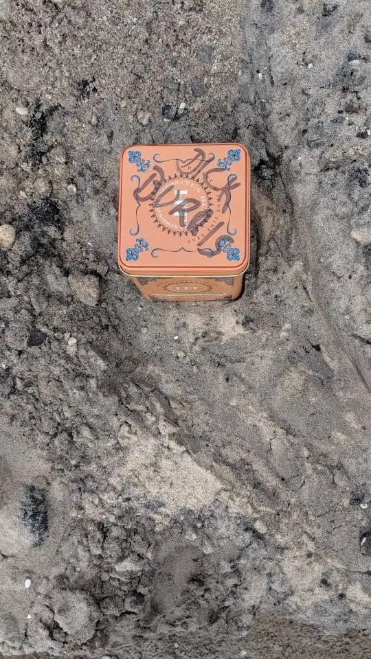 A small orange decorative metal tin rests on a rough gray surface.