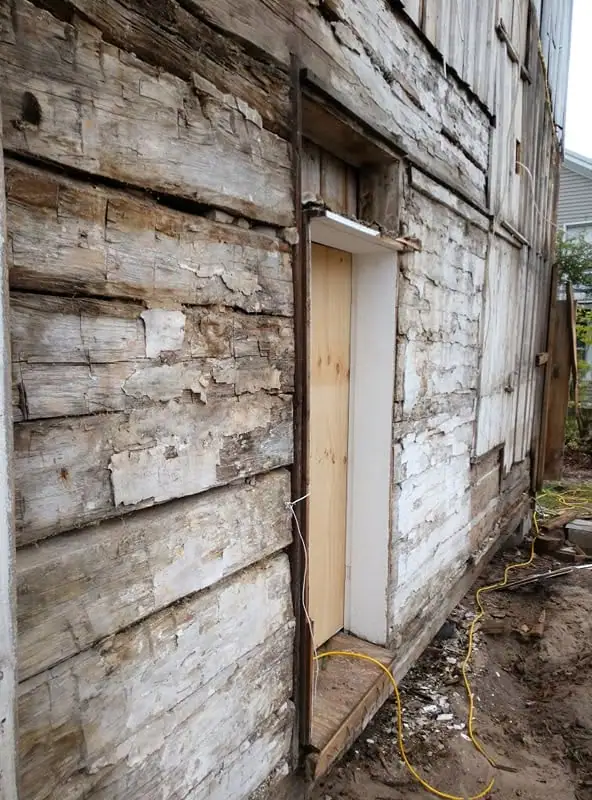 Close view of a severely weathered wooden building wall with a narrow doorway and yellow extension cord.