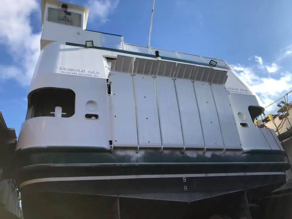 Low-angle view of a white vessel with a dark hull, deckhouse, railings, and large side doors.