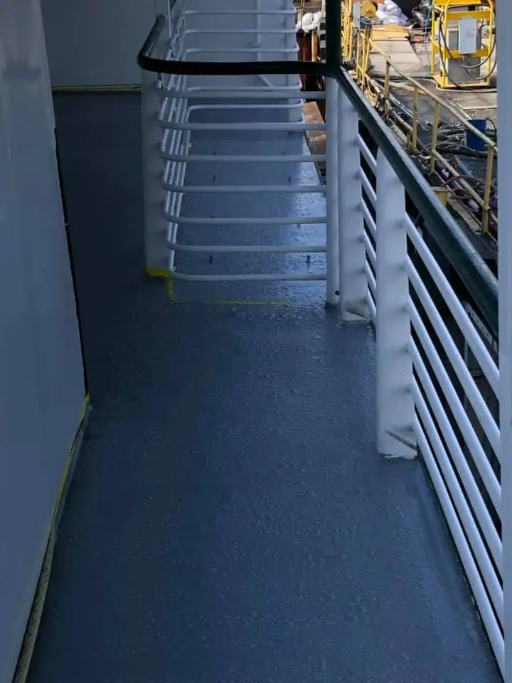 A narrow vessel deck passage with white railings and yellow industrial equipment alongside.