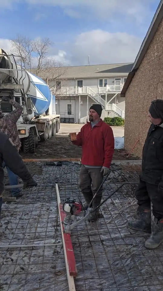 Workers stand beside a concrete mixer over a rebar-filled construction area.