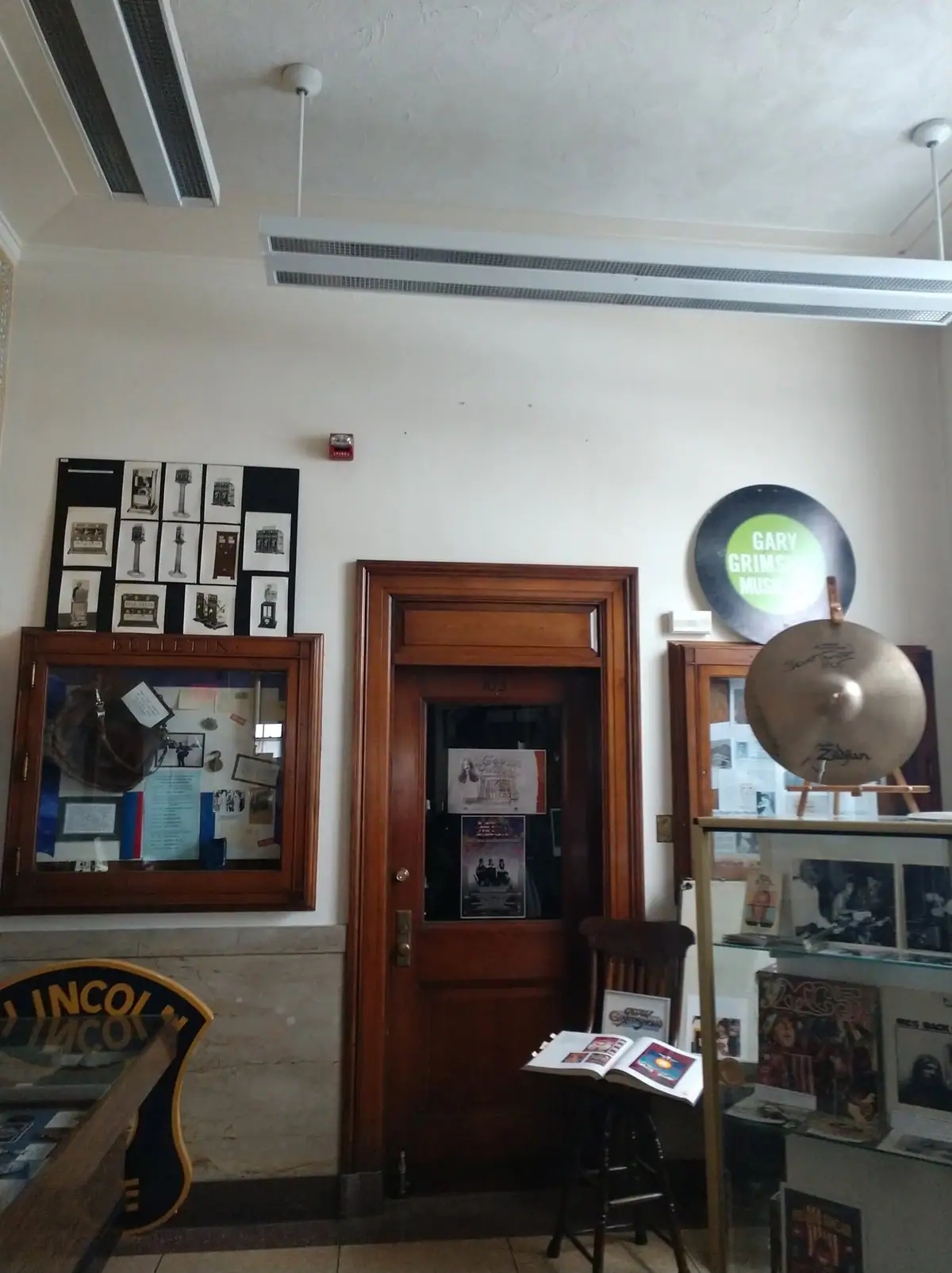 Museum interior with a wooden doorway, bulletin display, glass cases, and musical instruments.
