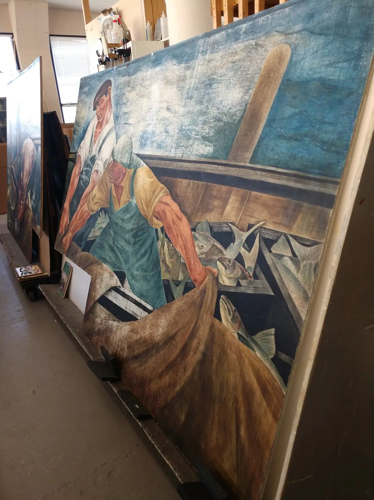 A large fishing mural with two fishermen and fish panels is shown inside a workroom.