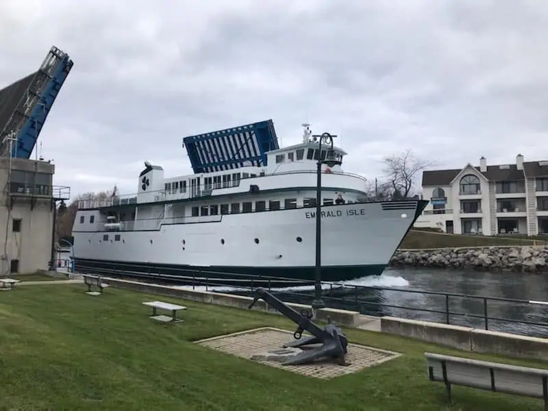 A white ferry marked EMERALD ISLE passes a waterfront park with benches and a large anchor.