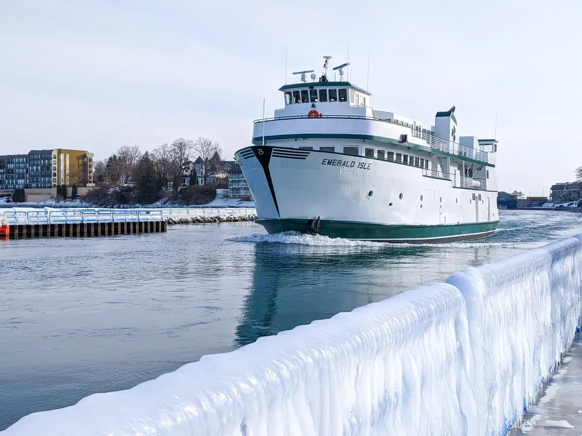 A white-and-green ferry passes an ice-coated pier in a winter harbor.