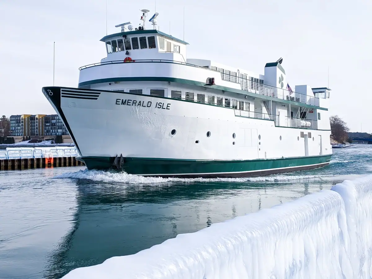 A white-and-green ferry moves through icy water beside a snow-covered dock.