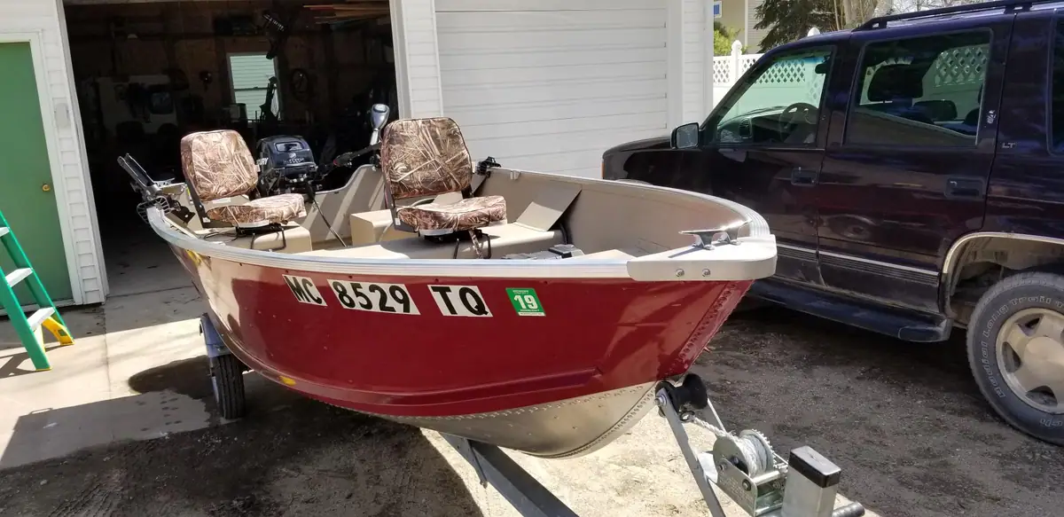 A red motorboat with two camouflage-patterned seats sits on a trailer beside a dark SUV.