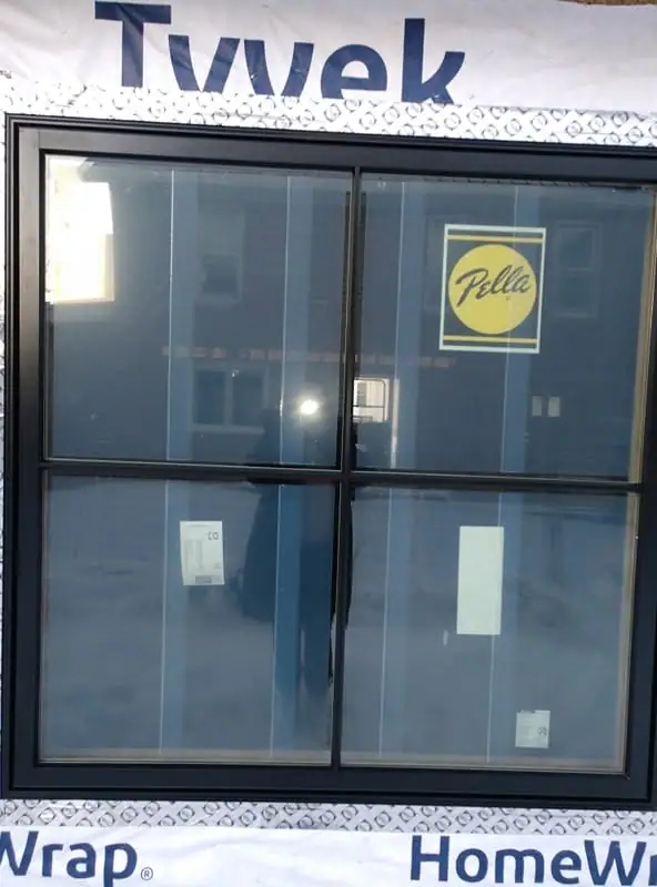 A four-pane window displays a yellow Pella logo within a black frame beneath large blue lettering.