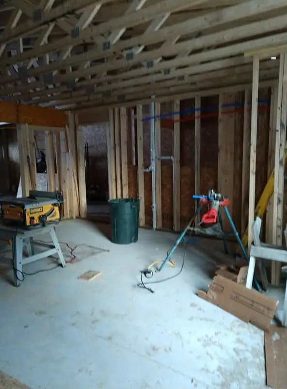 Interior construction scene with exposed wood framing, tools, a green bin, and a concrete floor.