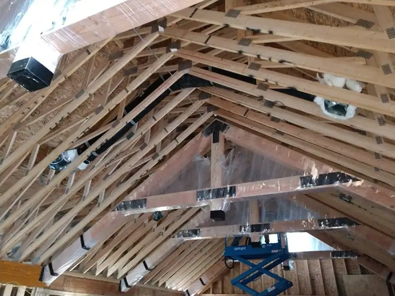 Wood-framed building interior under construction, with exposed roof trusses and a blue scissor lift.