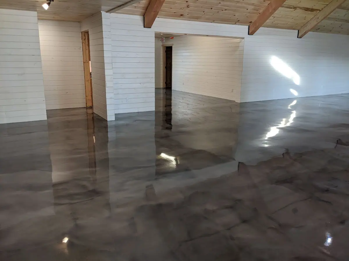 Empty room with white paneled walls, exposed beams, doorways, and a highly reflective concrete floor.