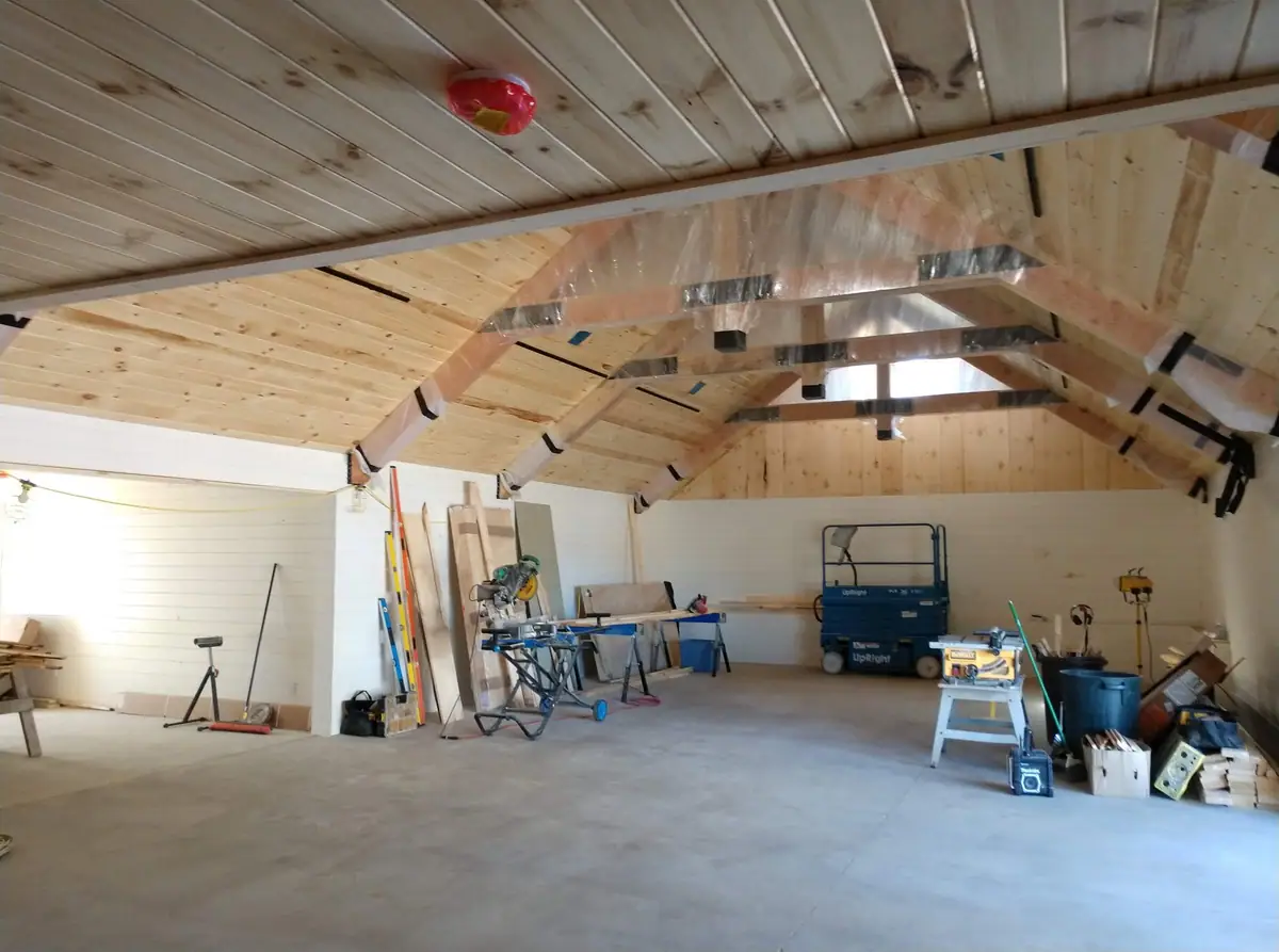 Interior of a wood-paneled workshop with construction tools, worktables, and a blue lift.